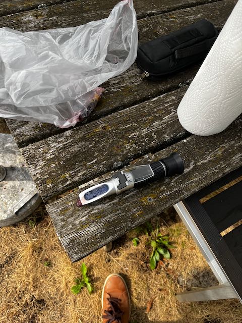 Handrefraktometer auf einem verwitterten Holztisch, daneben der Beutel mit der Probe